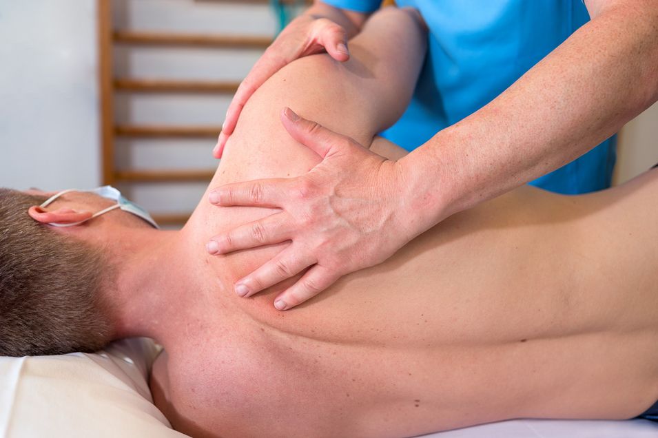 A patient is lying topless sideways on a couch and the physical therapist is examining the patient's right shoulder.