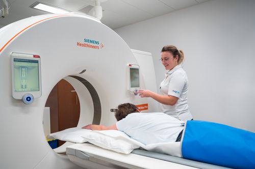Eine Radiologiefachperson bedient den Computertomographen (CT) und spricht mit einer Patientin.