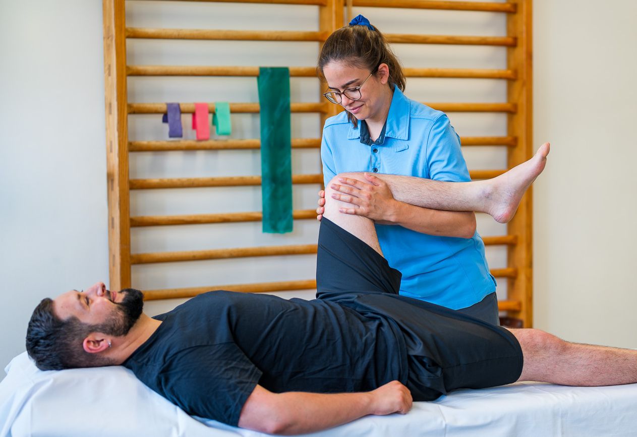 The physical therapist examines a patient's left knee while he is lying on his back on a couch with his knee bent.