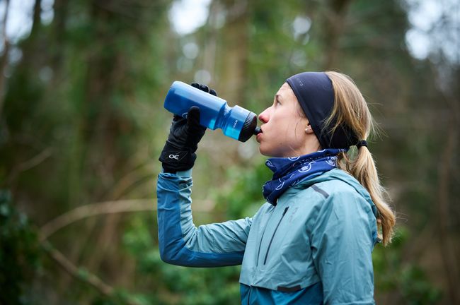 Eine Joggerin trinkt aus einer Flasche beim Joggen im Wald.