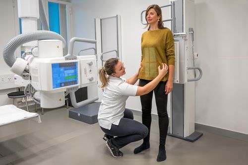 Vor der Röntgenuntersuchung der Lendenwirbelsäule positioniert die Radiologiefachperson die Patientin am Röntgengerät.