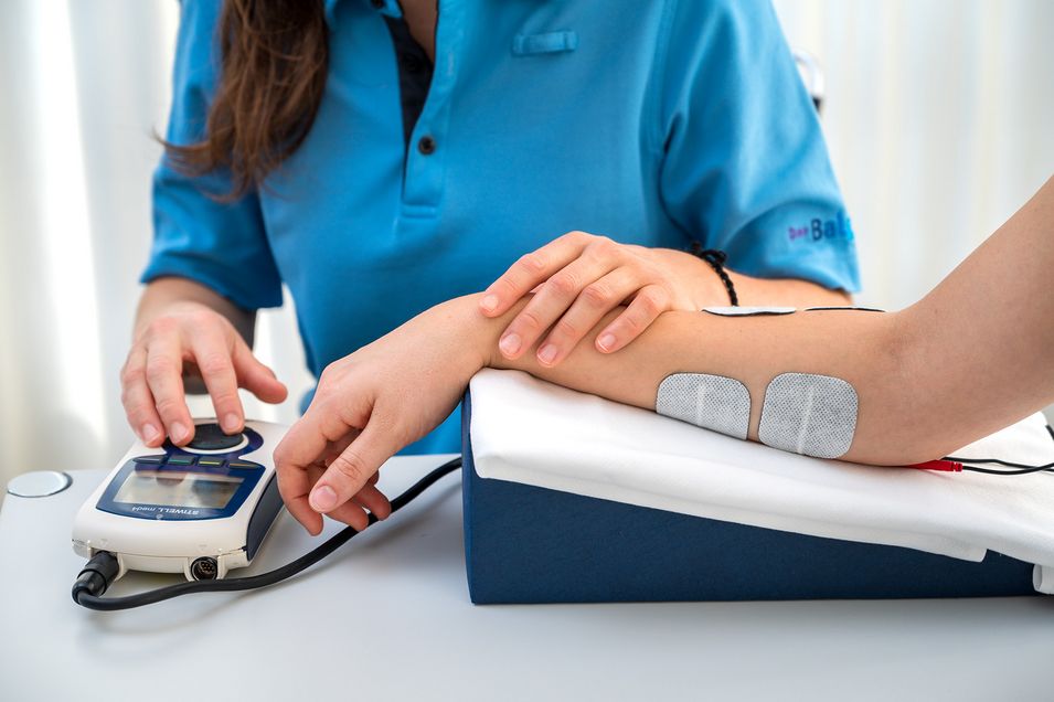 Muscle stimulation via skin electrodes on a patient's arm.