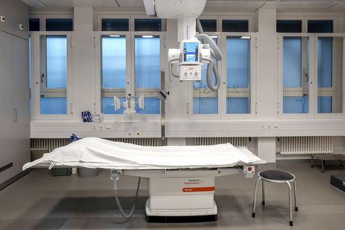 The X-ray machine and the examination couch below can be seen in a room with windows.