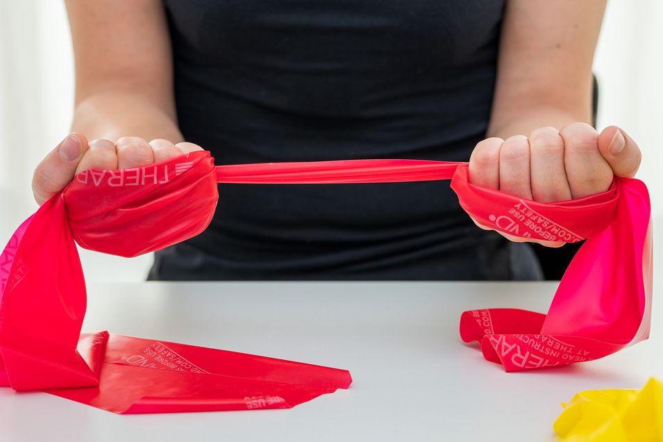 Close-up of a patient holding a red theraband in both hands and pulling it taut.