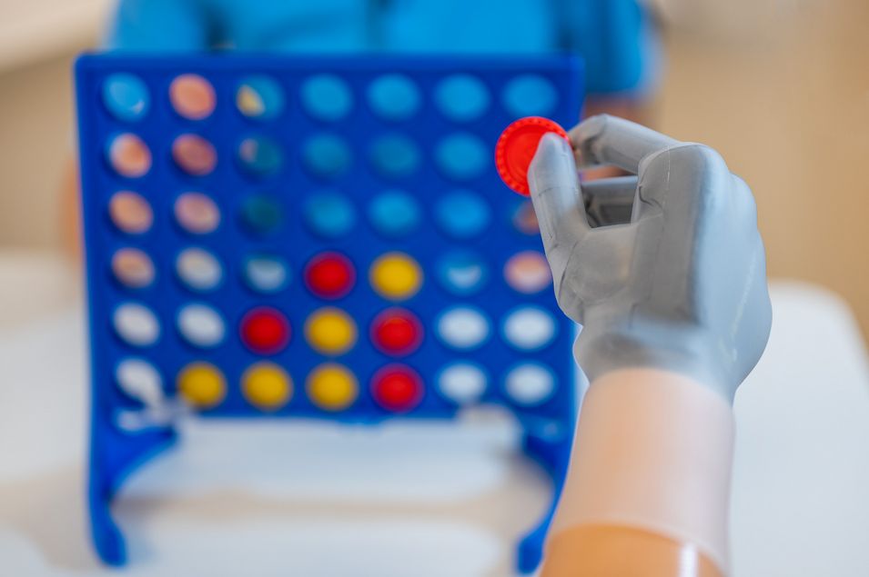 A man holds a red token with his prosthetic hand in the game "Connect Four".