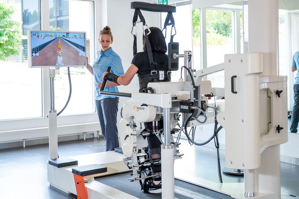 Patient on the treadmill and clamped up to the waist in the Lokomat, looking at the screen, which shows a male running straight ahead from behind.