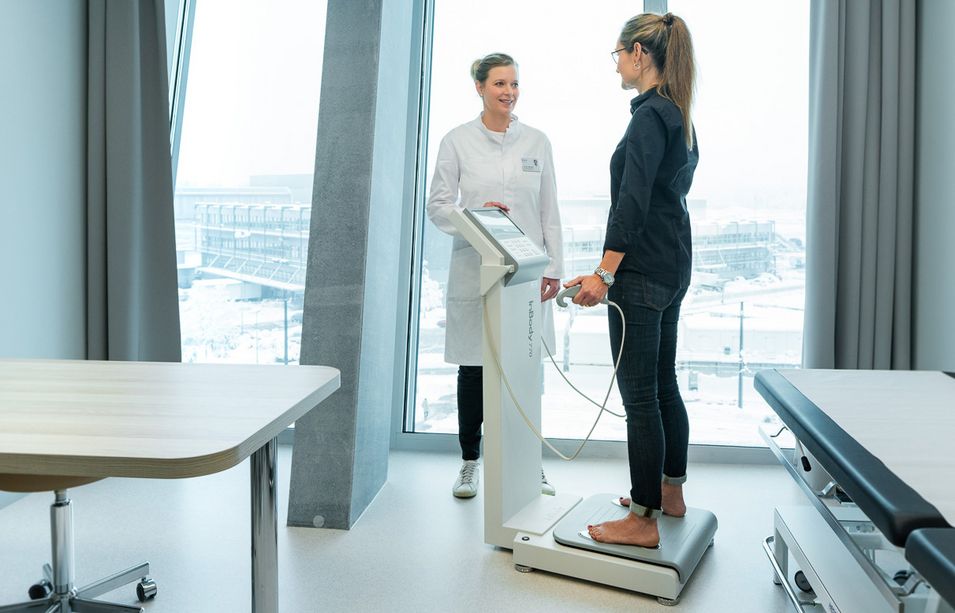 The patient is standing on a functional device and the doctor is operating the device.