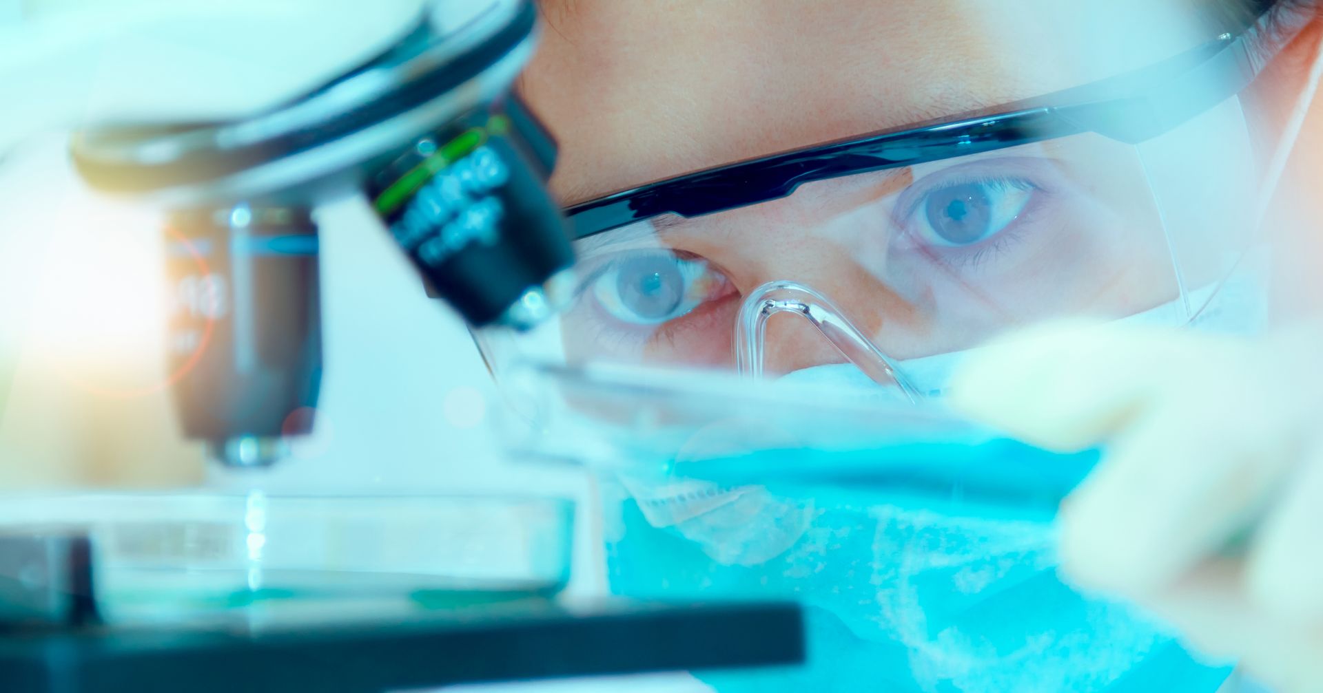 A researching person wearing protective goggles examines something with a laser.