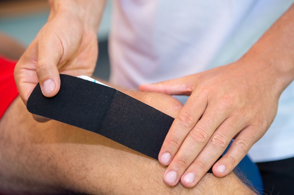 Close-up of a male knee to which a physiotherapist is applying a tape.