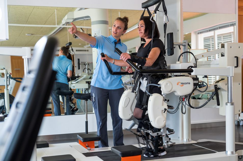 Patient on the treadmill and clamped up to the hip in the Lokomat, is instructed by the physiotherapist.