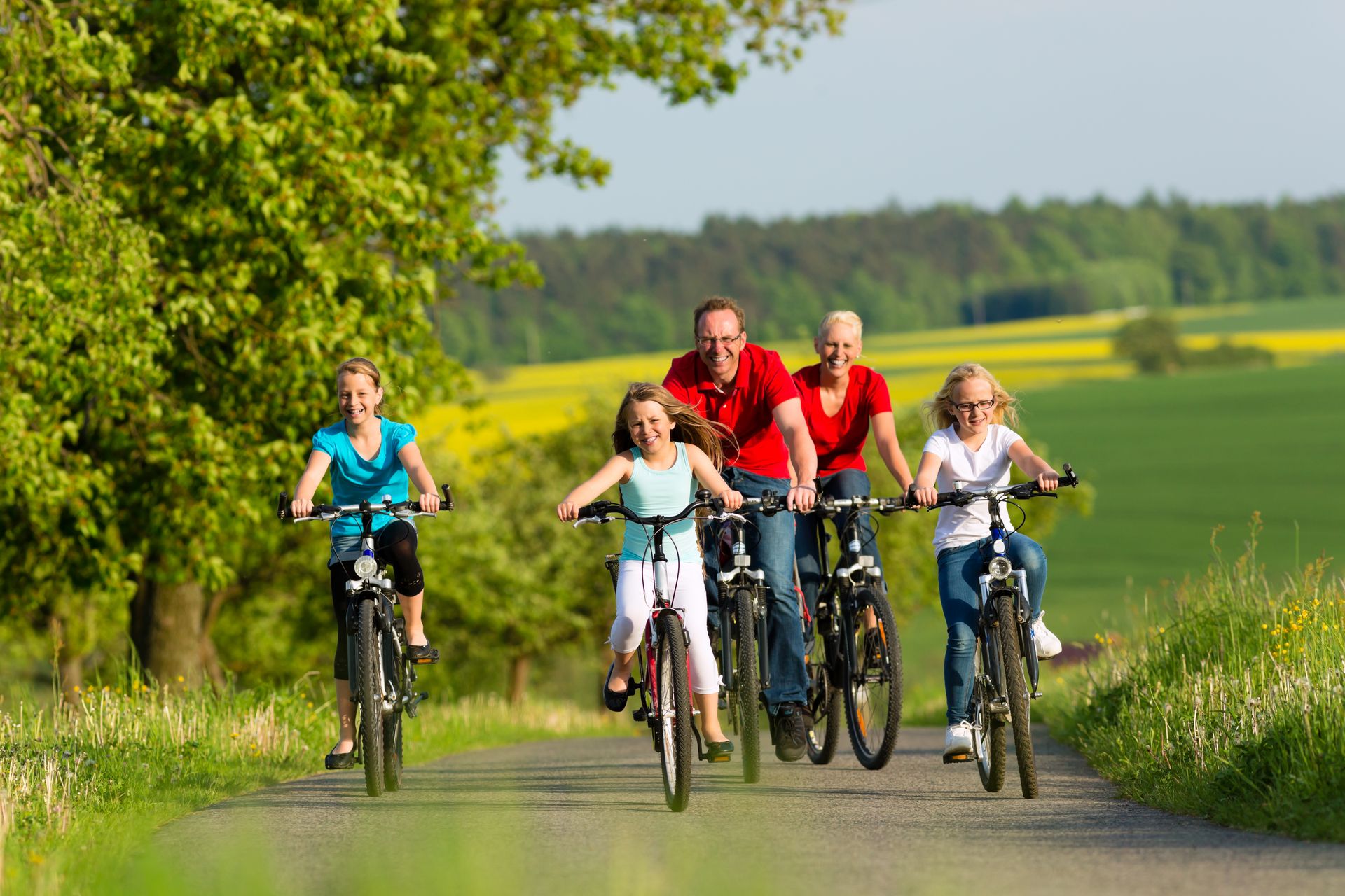 Familie fährt mit dem Fahrrad auf einem Feldweg über grüne Wiesen..
