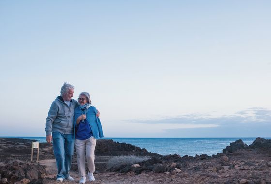 Ein älteres Liebespaar macht sich Gedanken über eine Hüftoperation beim Spazieren am Meer.