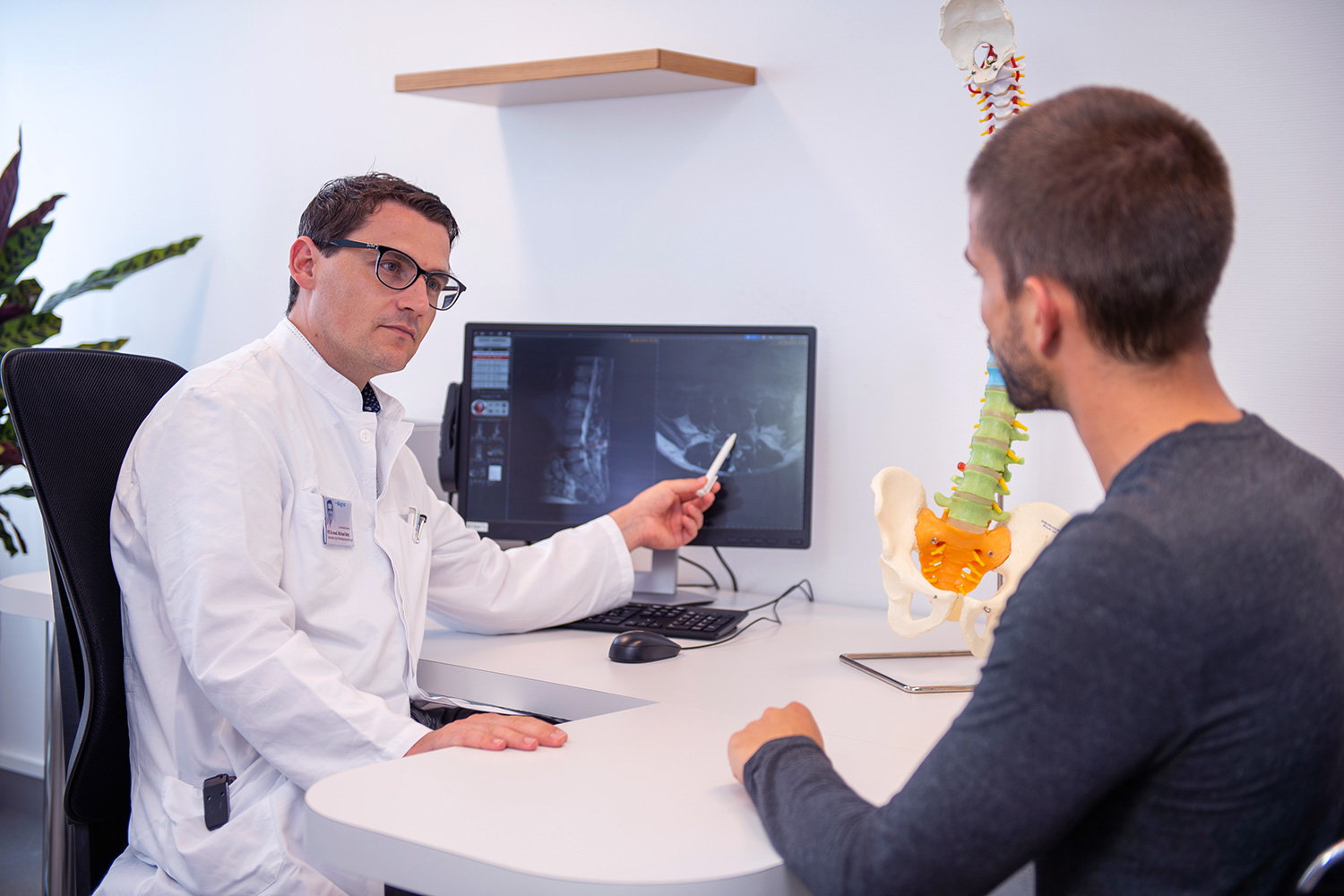 Ein Wirbelsäulenarzt erklärt dem Patienten in der Sprechstunde das Röntgenbild am Computer.