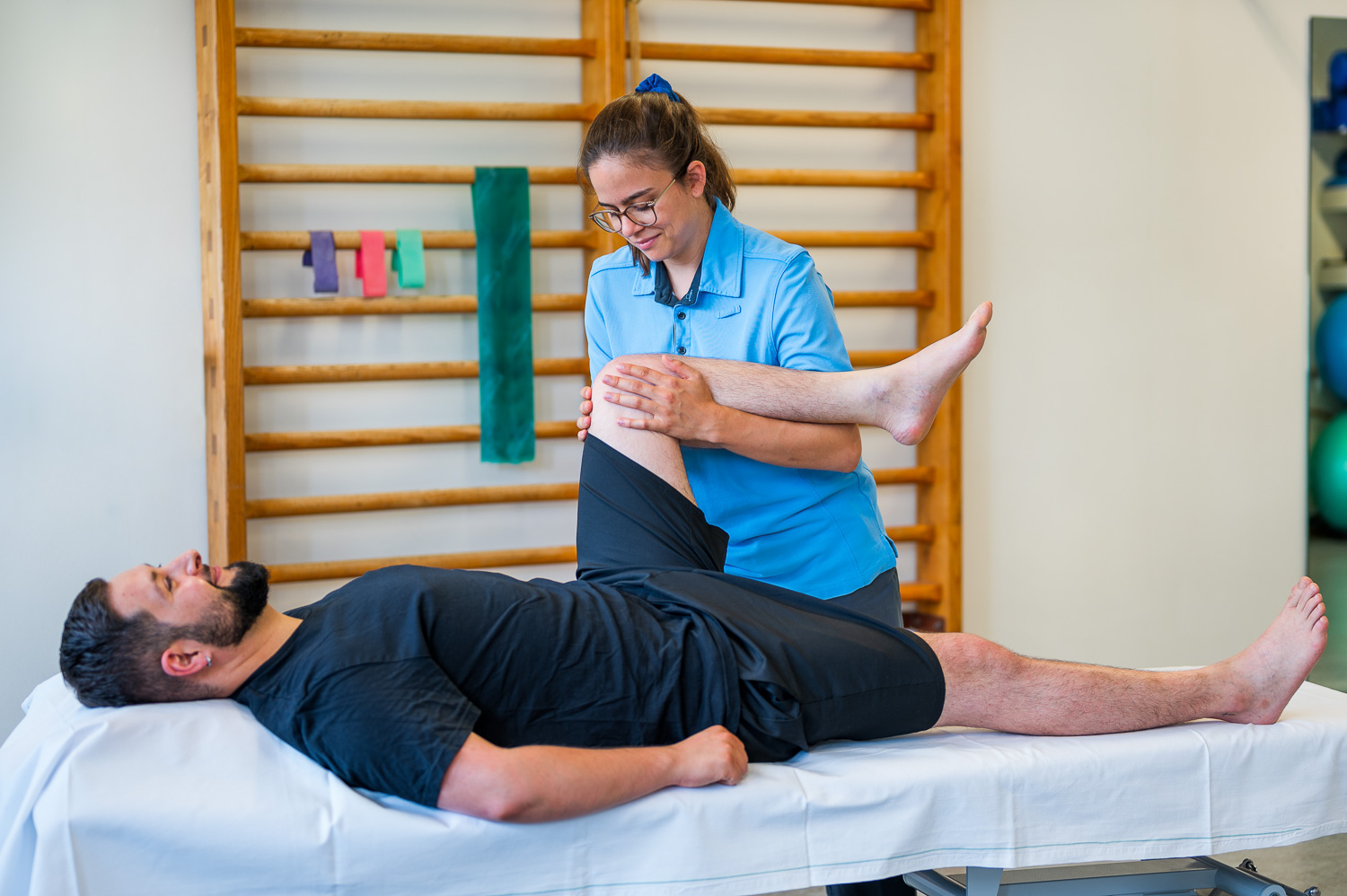 The physical therapist examines a patient's left knee while the patient is lying on his back on a patient couch.