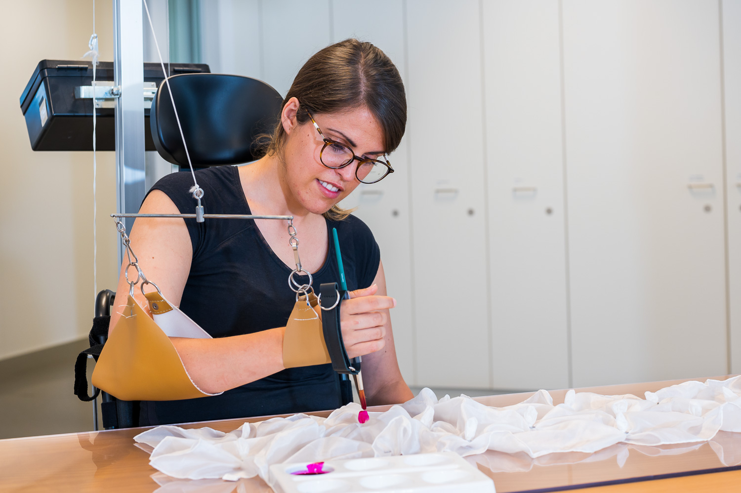 A patient holding a brush with the help of a device and using it to paint on fabric.