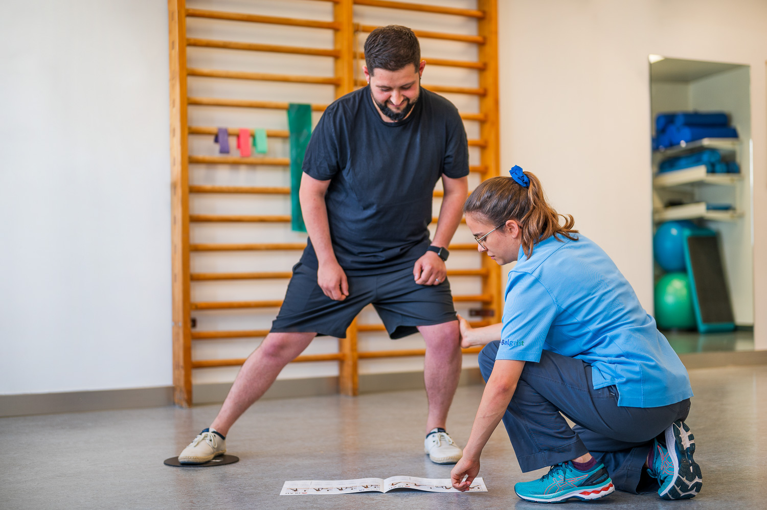 Physical therapist instructs standing patient performing a lateral lunge to the right.