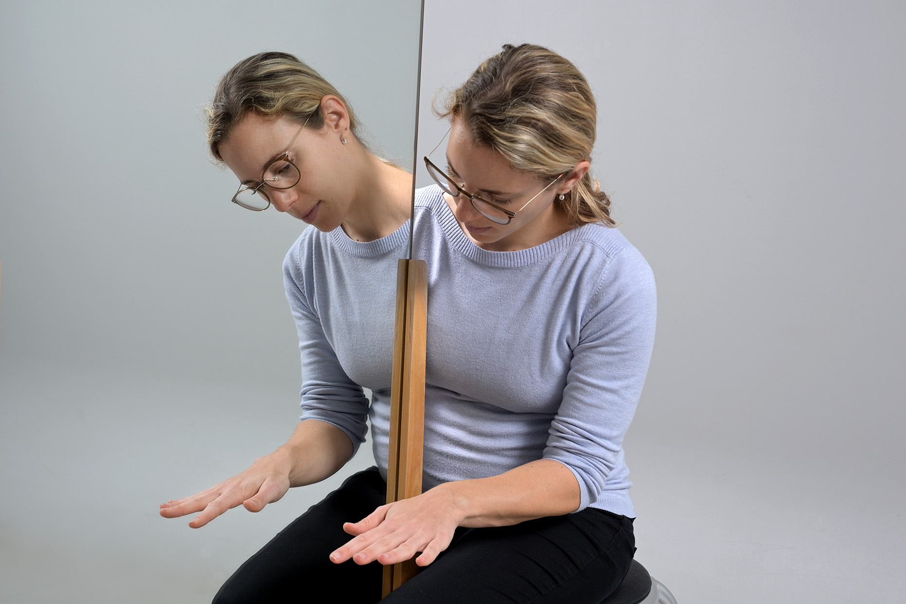Eine vor einem Spiegel sitzende Frau erlernt die schmerzfreie Bewegungen der Hand mithilfe eines Spiegels.