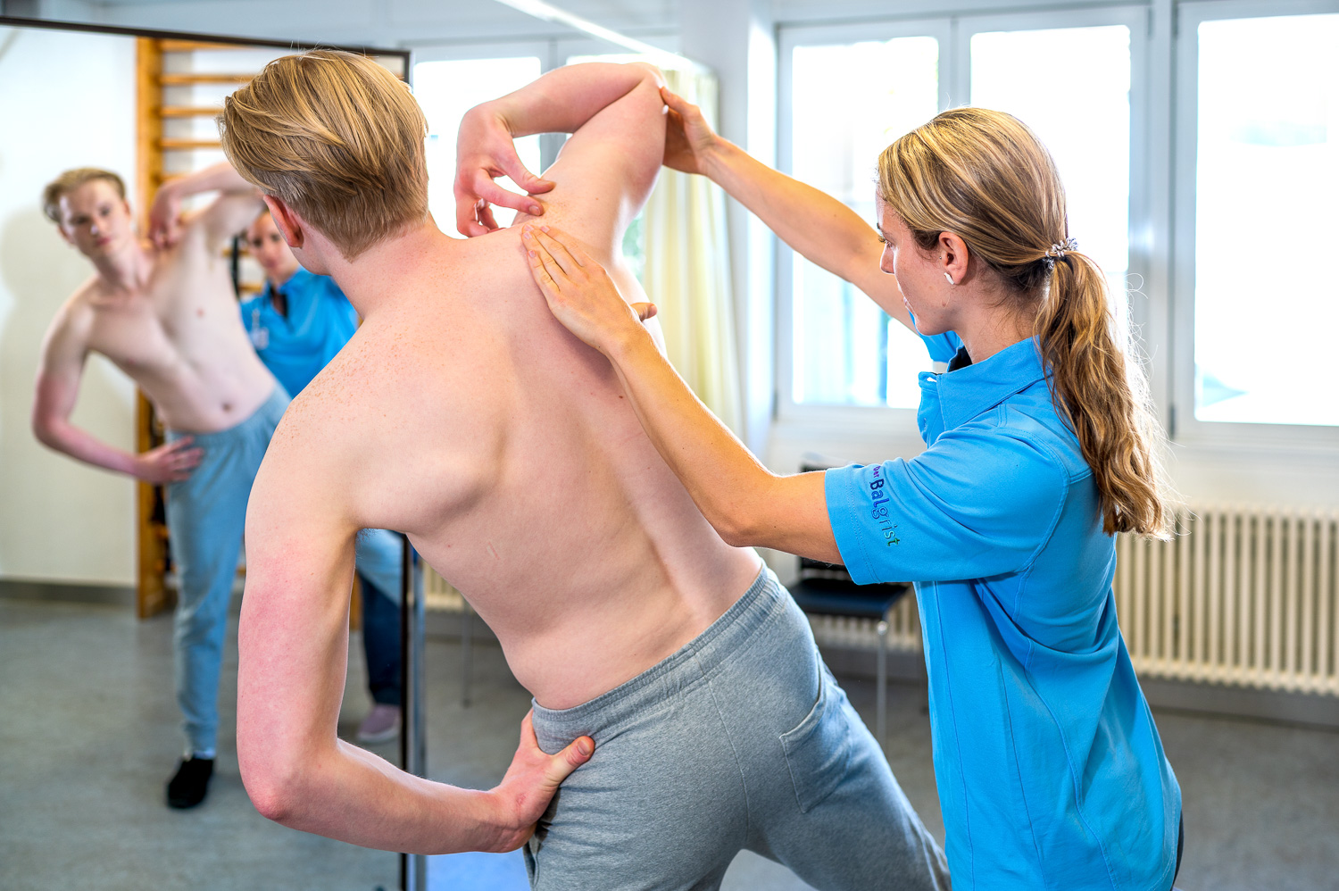 A physiotherapist is doing exercises with the patient in front of a mirror.